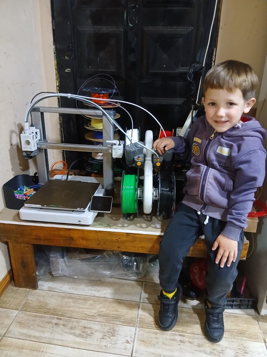 Amadeo sonriendo sentado junto a la impresora 3D y los rollos de filamento de colores